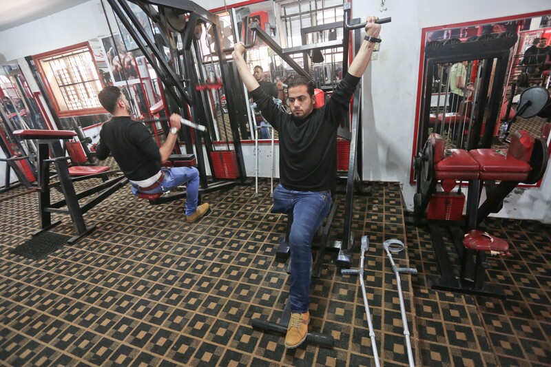 Two young men lift weights at a gym