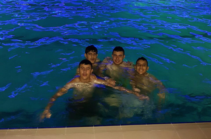 Four boys pose for camera while in a swimming pool