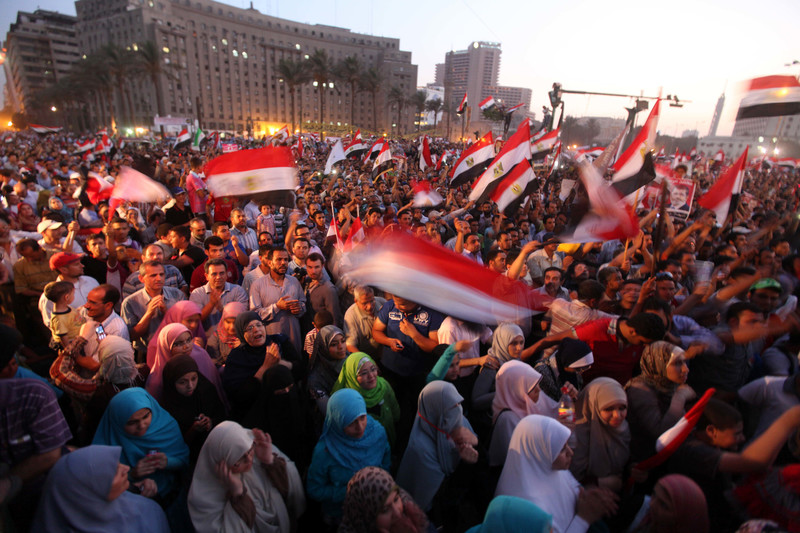 Crowd of dozens of men and women waving Egyptian flags