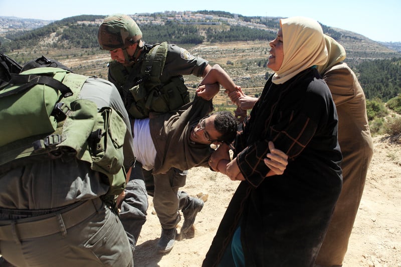 Two Israeli soldiers carry Basil al-Araj as women attempt to stop them