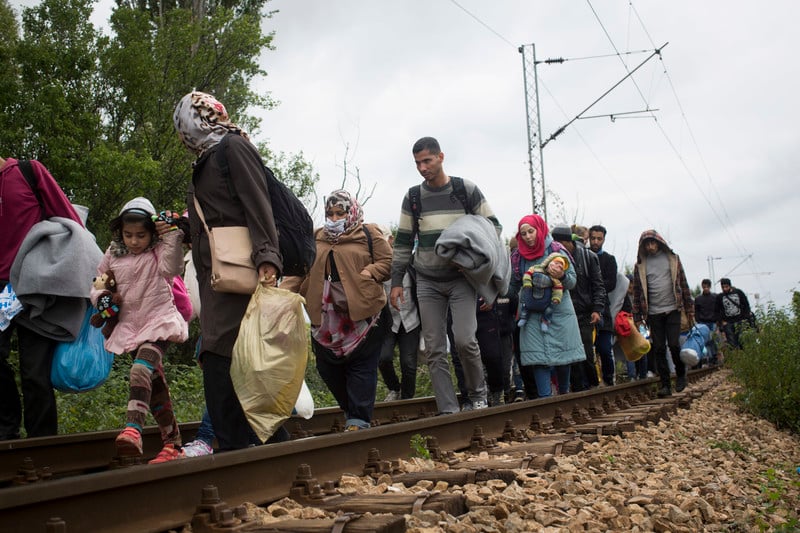Men, women and children walk along railroad tracks while carrying their belongings