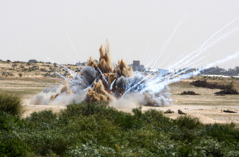 Photo shows explosion causing a plume of dirt and streaks of white smoke with burning tips 