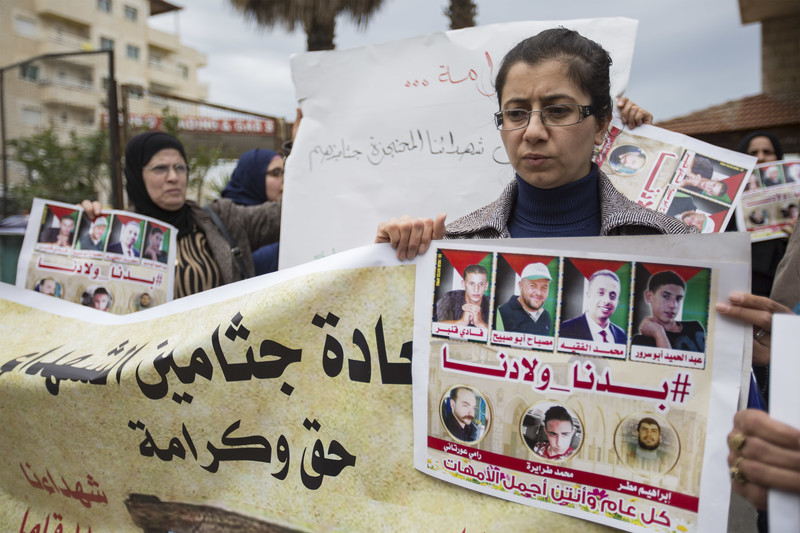 A woman holds a banner and a poster showing photos of slain men whose bodies are being held by Israel