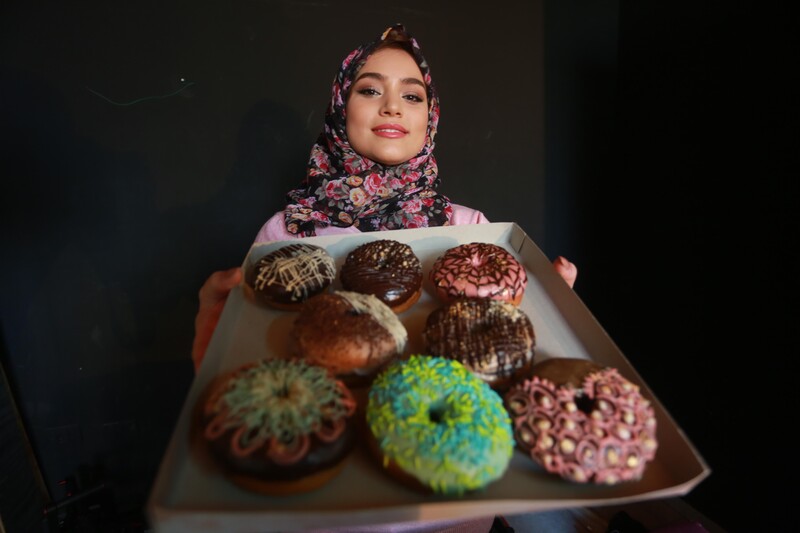 Young woman holds up a tray of doughnuts with varying toppings