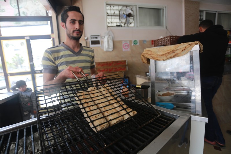 Man holds up grill press holding several falafel sandwiches