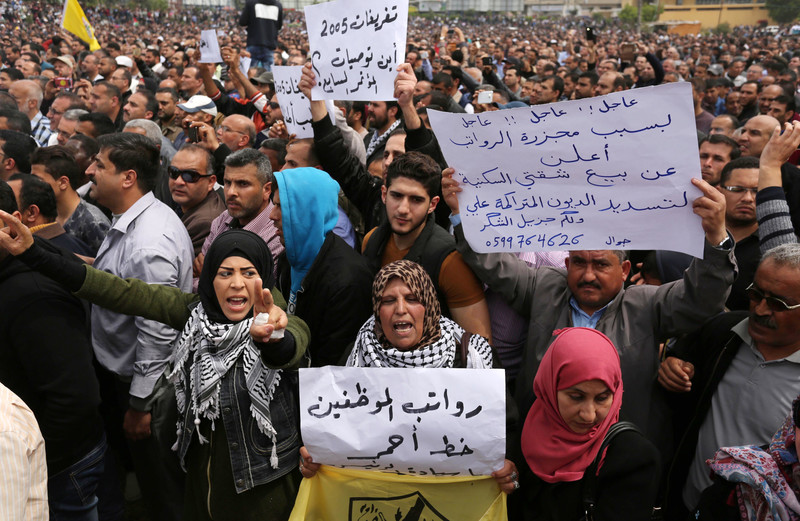 Men and women hold Arabic-language signs protesting salary cuts during large demonstration