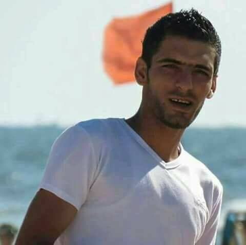 Young man in t-shirt is seen from chest up standing in front of sea