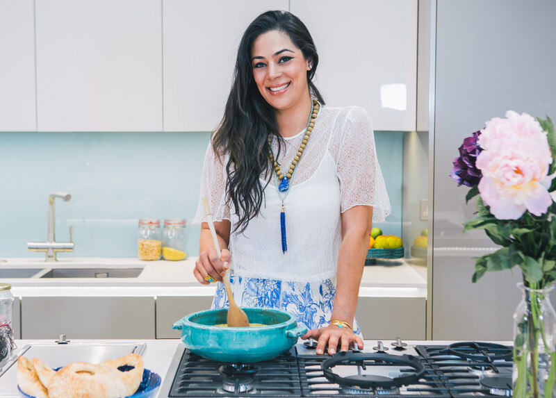 Smiling young woman seen waist-up standing behind kitchen counter while stirring pot on a stovetop