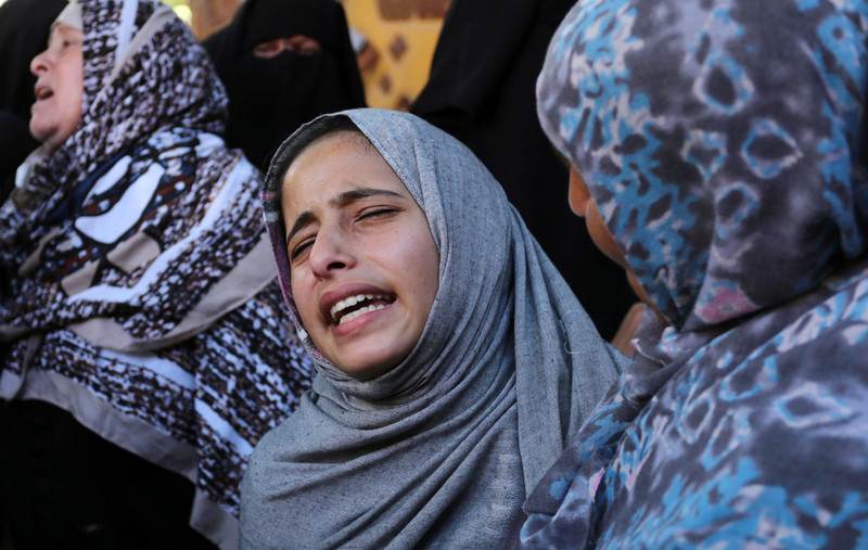 Girl wearing head scarf, seen from shoulders up, is comforted by woman while she cries