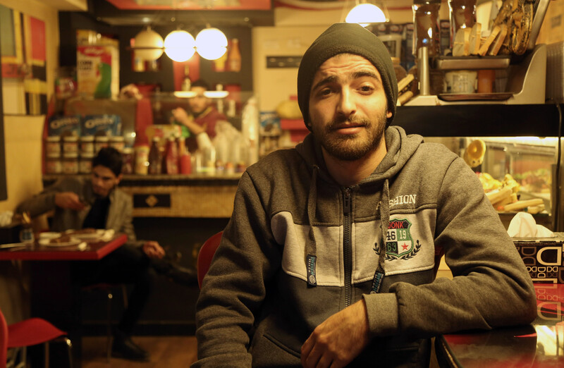 Young man wearing hoodie and knitted hat sits in cafe