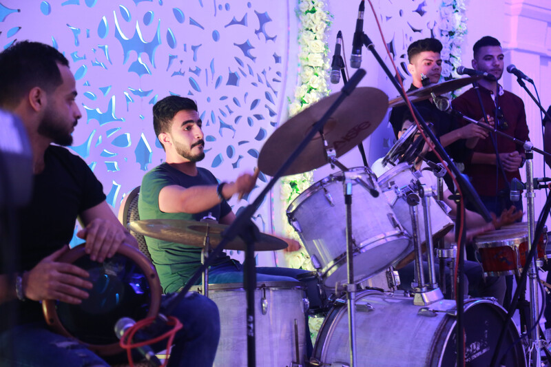 Close-up on young man playing on a drum kit with a tabla player and two singers standing on either side of him