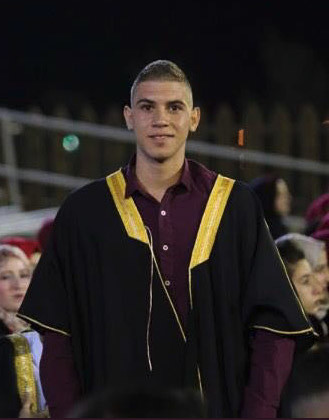 Photo shows smiling young man wearing graduation ceremony gown from waist up