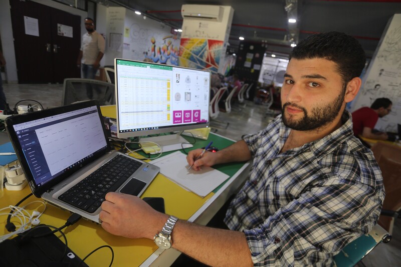 Young man sits at desk with a laptop and external monitor in front of him