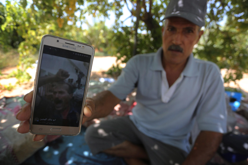 Man sitting on ground in vineyard shows photo on his phone