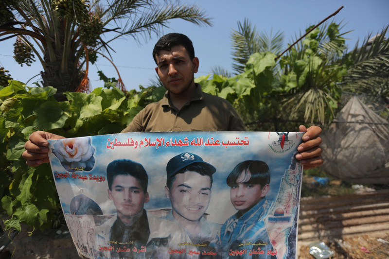 Man, seen from chest up, holds poster showing images of three youths and a rose representing slain woman