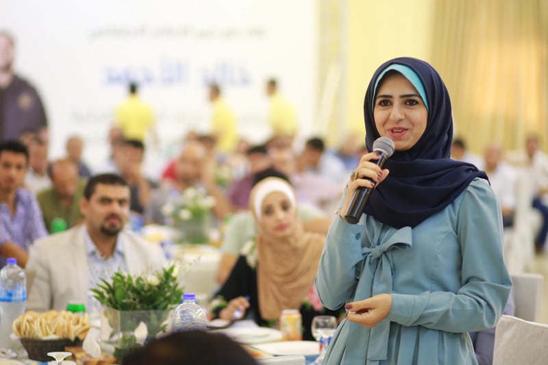Young woman seen from waist up speaks into a microphone in a banquet hall