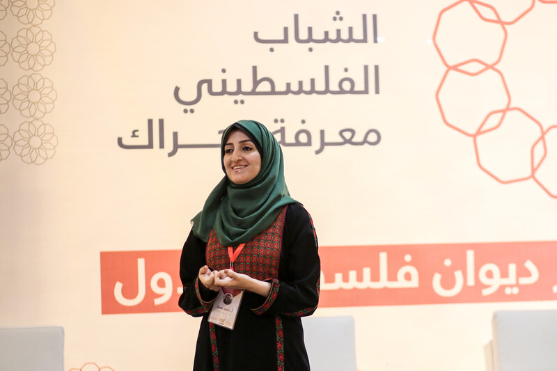 Smiling young woman seen from waist up stands on a stage.