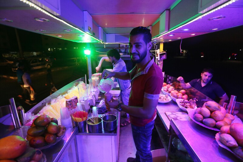 Smiling young man pours smoothie mix into a plastic cup at an outdoor juice stand