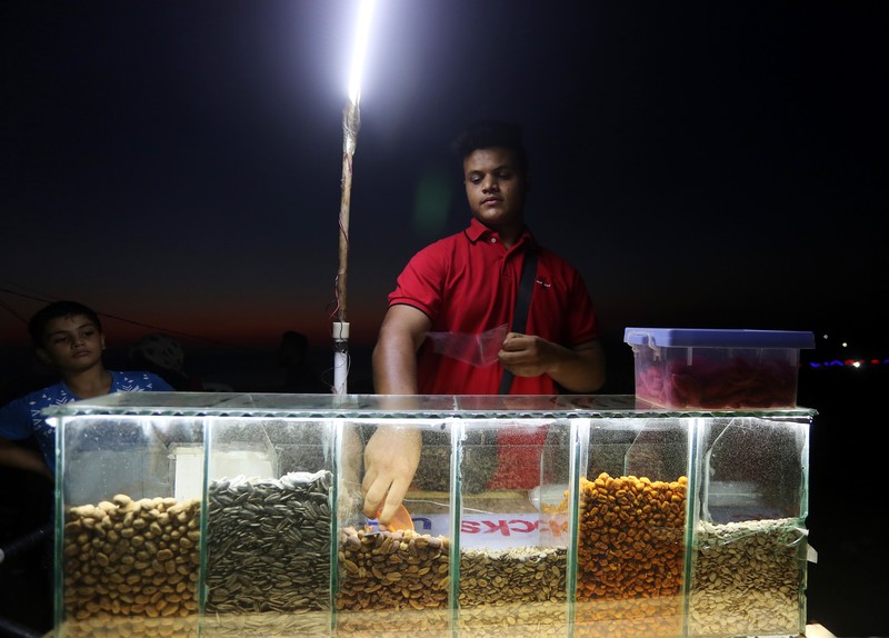Young man seen from waist up scoops nuts at outdoor booth at nighttime