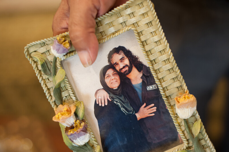 Photo shows hand holding framed photograph of older woman embracing younger son wearing prison uniform