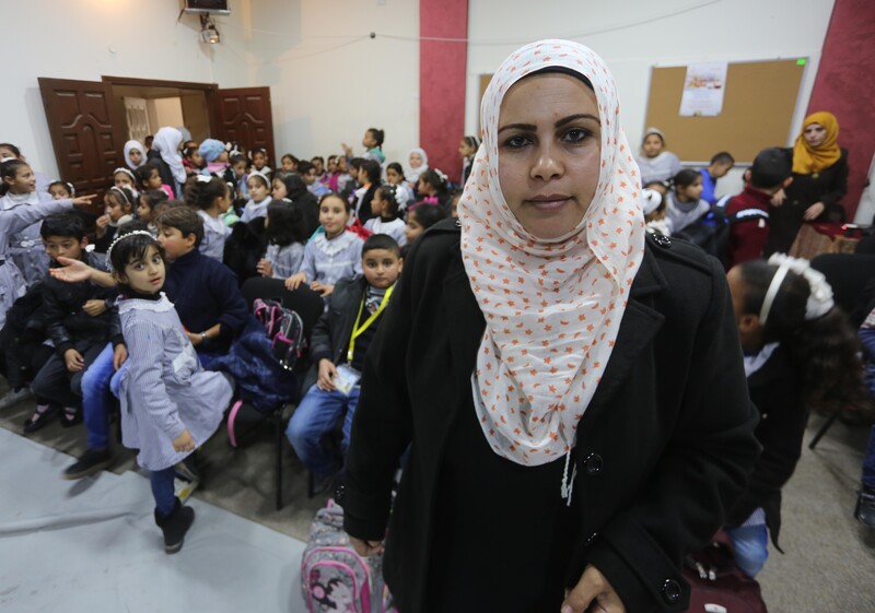 A young woman looking at the camera stands in front of a crowded hall of schoolchildren