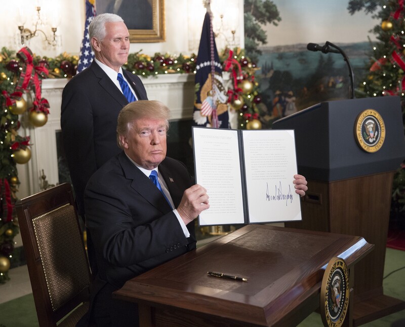 Trump sits at desk holding up newly signed executive order as Vice President Pence stands behind him