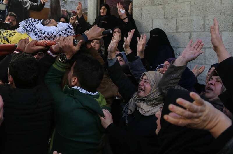 Photo shows crying women waving their hands at shrouded body of young man being carried on stretcher