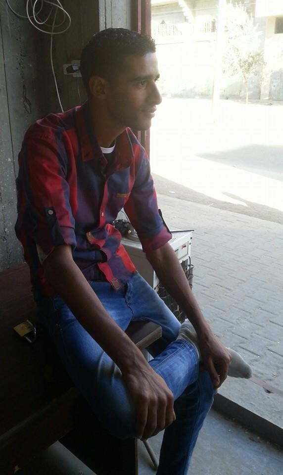 Photo shows young man sitting on chair looking out onto sunny street