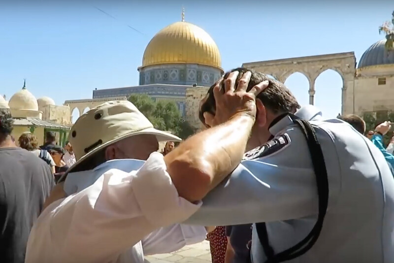 Policeman puts his hands on man's neck as man puts hands on policeman's head