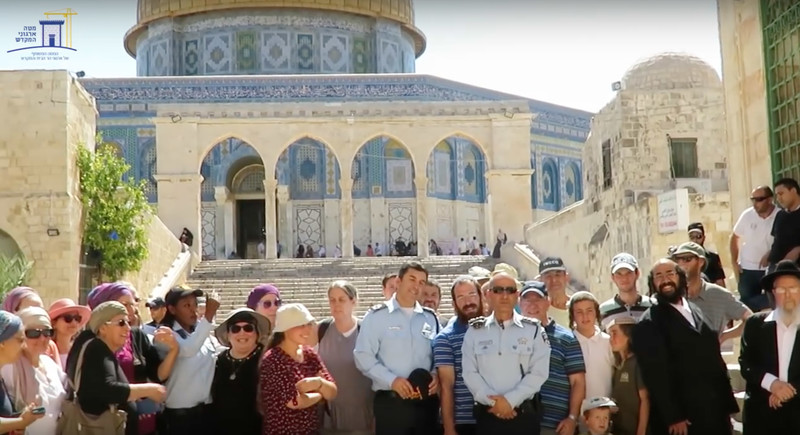 Three Israeli police are seen standing with group of civilians in front of stairs leading up to the Dome of the Rock