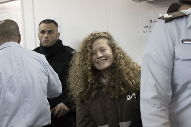 Ahed Tamimi, wearing prison uniform, smiles while surrounded by police