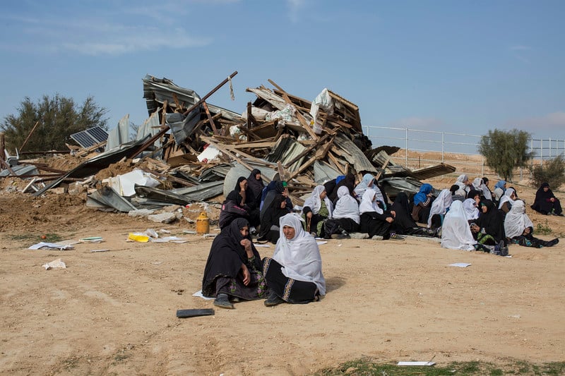 Several women sit in front of pile of debris 