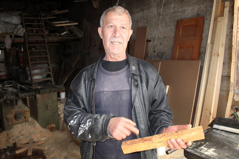 Man wearing leather jacket points to a piece of wood he is holding