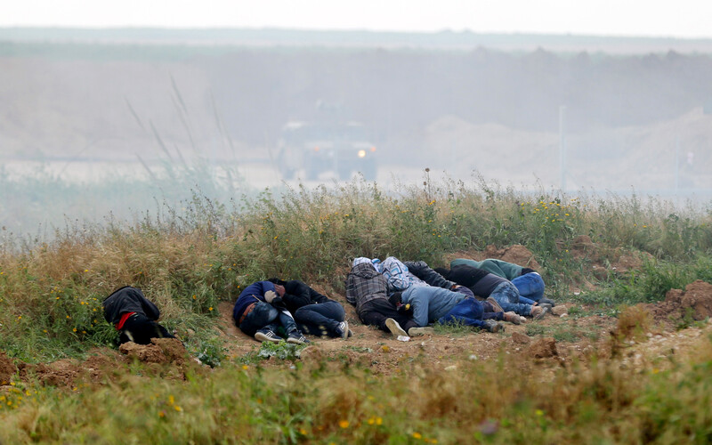 Youths take cover in embankment with Israeli military jeep and soldiers in background