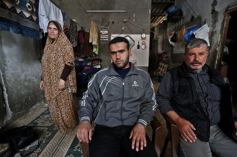 Father and son sit in chairs as mother stands behind them next to clothing line