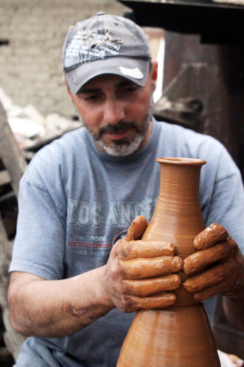 Man wearing baseball cap shapes a wet clay vase with his hands