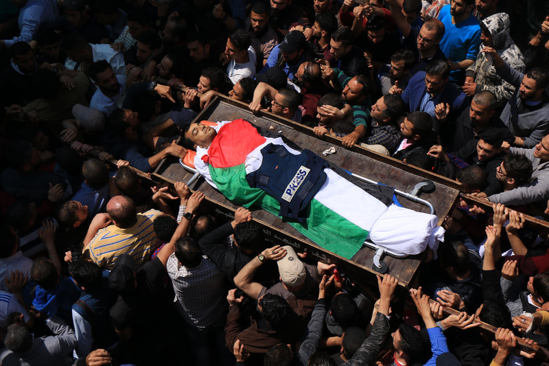 Crowd carries body of man shrouded in Palestinian flag with flak jacket marked PRESS laid on his body