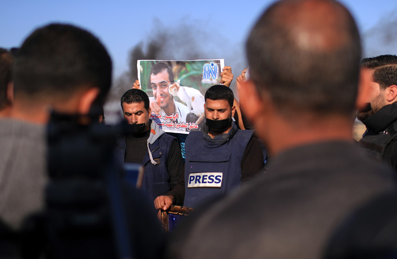 Protesters wearing flak jackets display poster of Yaser Murtaja holding a kitten