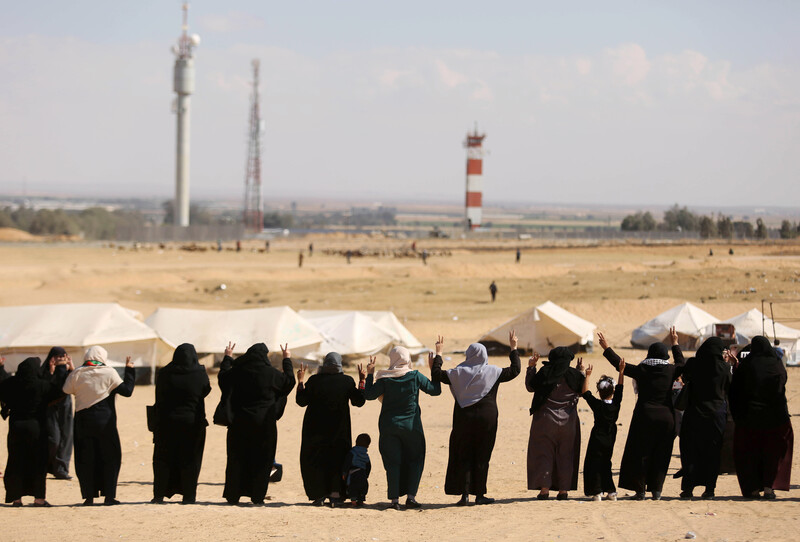Photo shows backs of women standing in a row making V for victory signs with their hands near the Gaza-Israel boundary fence