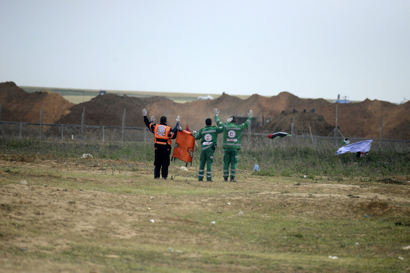 Three medics carrying a folded up stretcher put their arms in the air in front of Gaza-Israel boundary fence