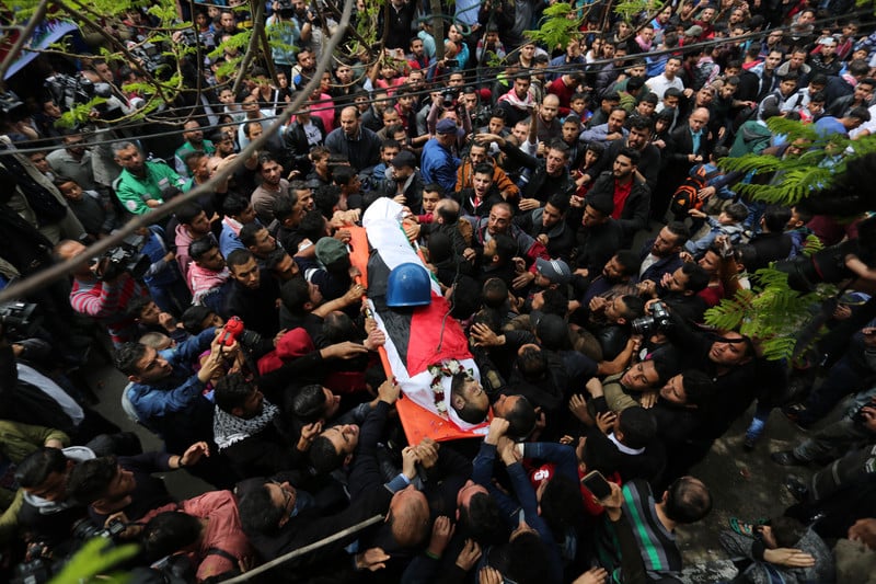 Body of journalist, wrapped in a Palestinian flag, is carried by a crowd of people with his protective helmet resting on him