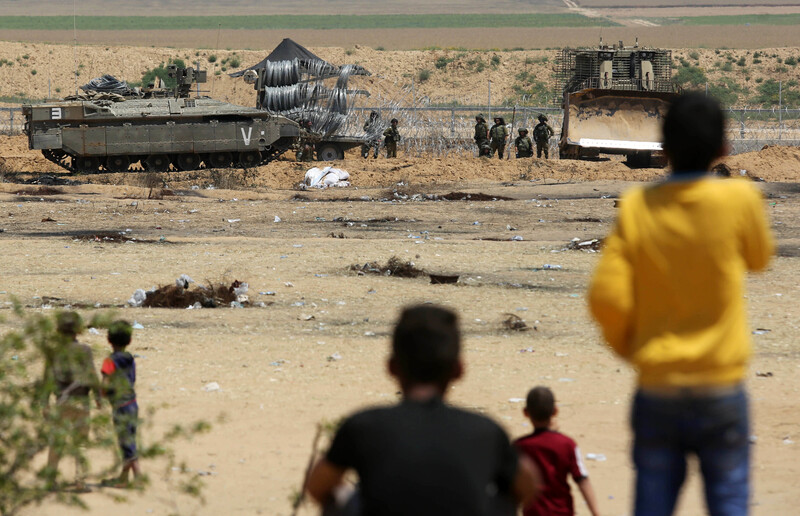 Photo shows backs of small children watching Israeli soldiers roll out barbed wire fence