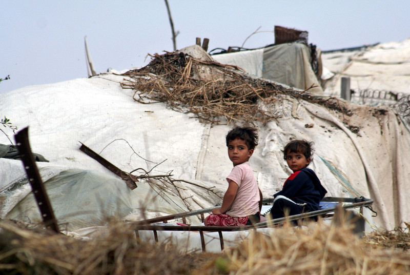 Photo shows small children sitting in front of tent shelter