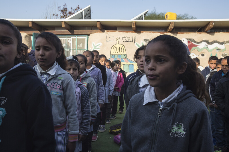 Schoolchildren stand in rows in front of single-story school