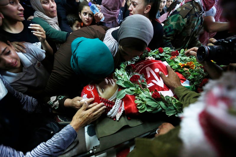 Women and girls mourn over body of youth wrapped in PFLP flags with a wreath placed on his torso