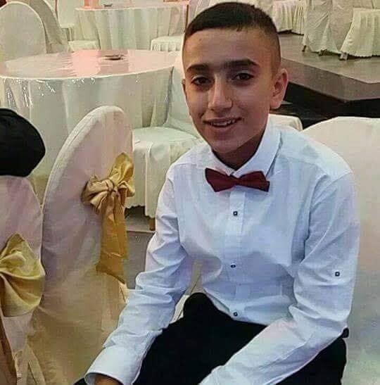 Smiling boy wearing dress shirt and bow-tie sits on chair in what appears to be a wedding hall