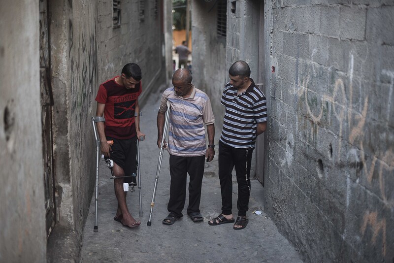 Three men stand in an alley, two of them using crutches.