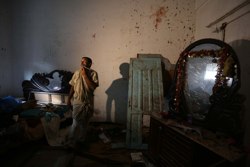 A man stands in the middle of a room with the walls splattered with blood