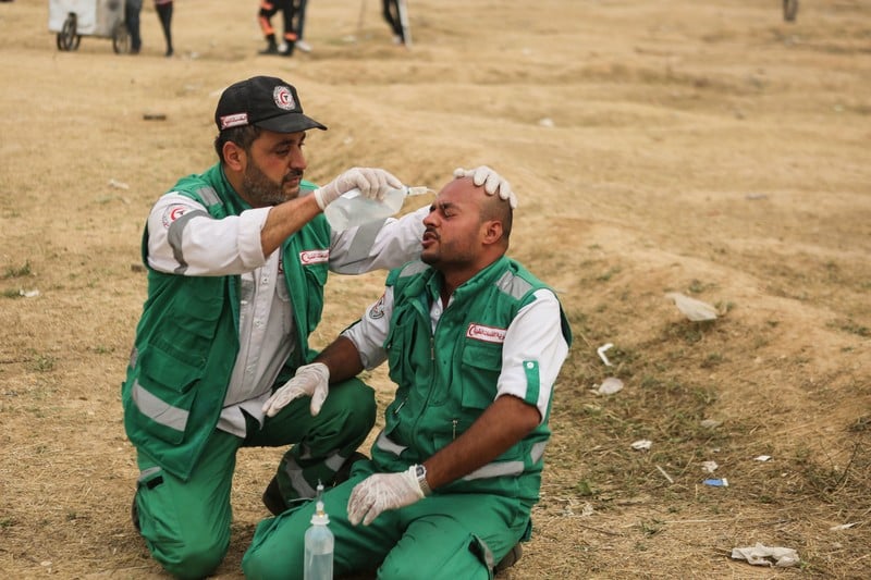 Adel al-Masharawi, kneeling on the ground while wearing paramedic uniform, pours liquid onto face of another paramedic sitting on the ground