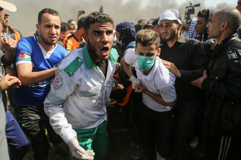 Young man in uniform stands in front of crowd as he helps carry injured person on a stretcher